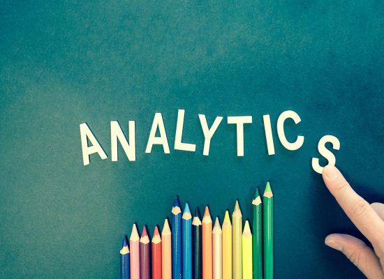 Colored pencils and letters spelling 'ANALYTICS' on a textured background with a hand.